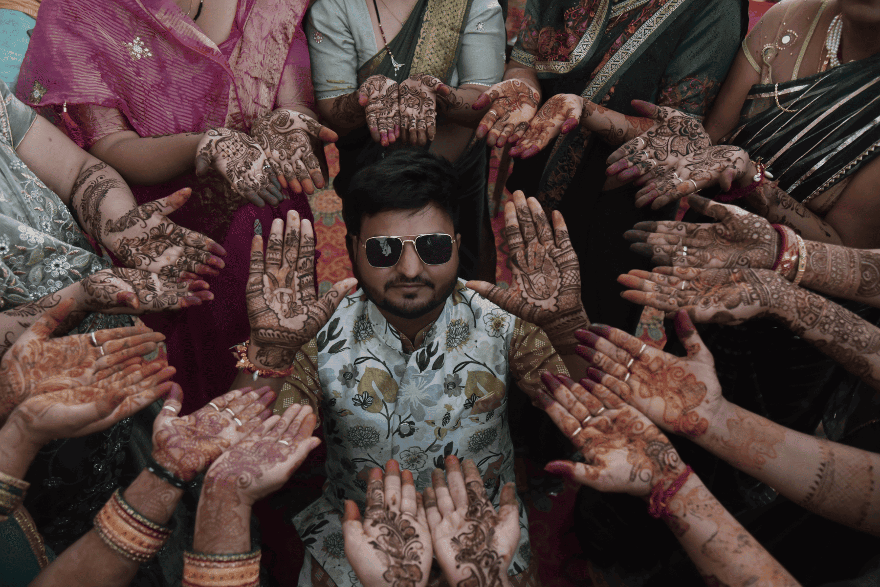 Groom's face framed between mehndi-covered hands of women during pre-wedding shoot